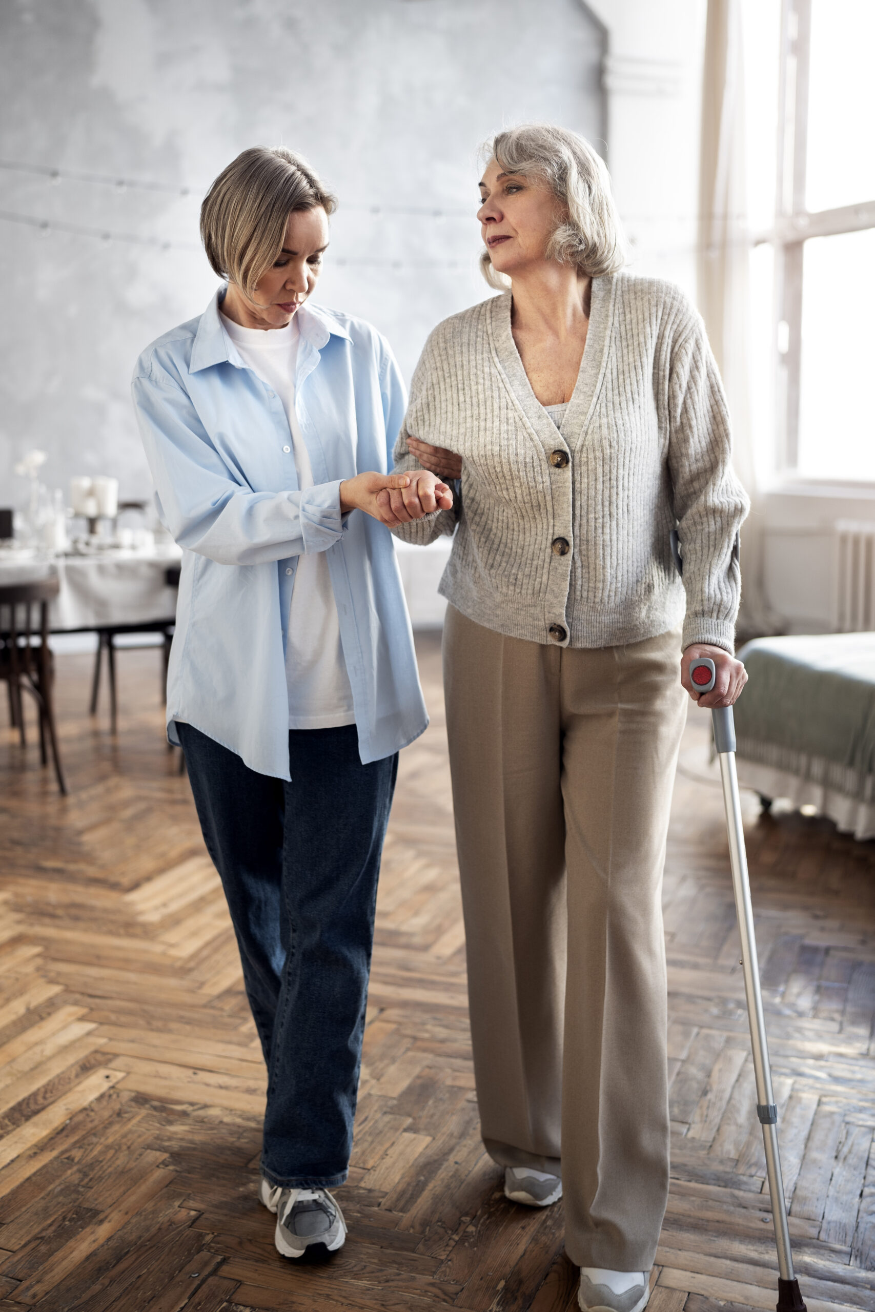Caregiver assisting an older adult using a walking stick to improve safety and prevent falls at home.