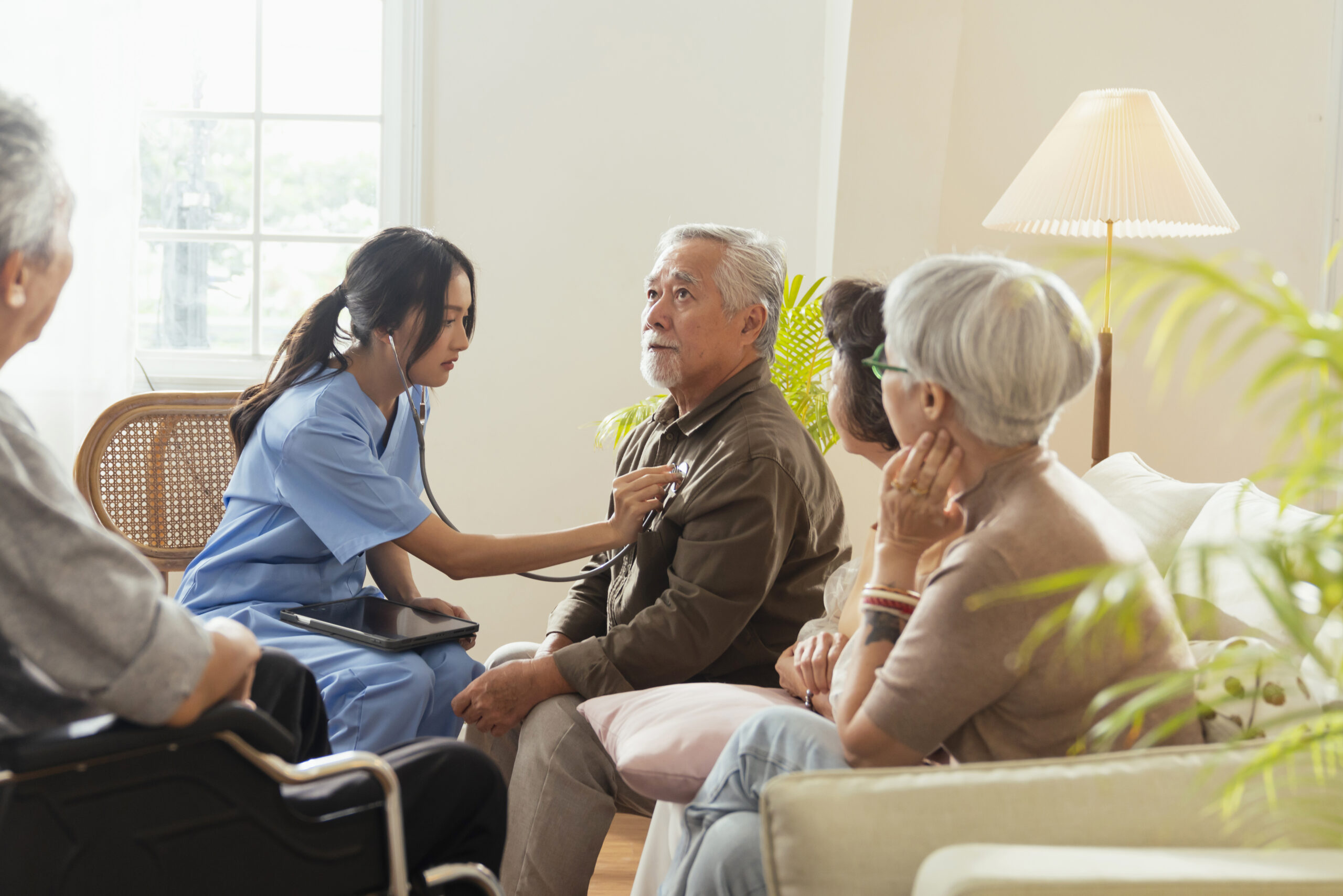 Healthcare professional assessing an elderly man at home while discussing NHS Continuing Healthcare (CHC) support with family members.
